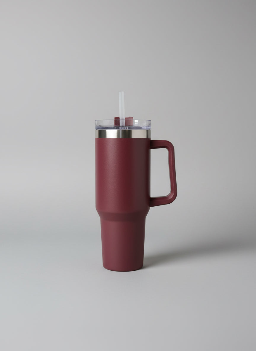 Pink thermos with a clear lid on a white surface with green leaves in the background