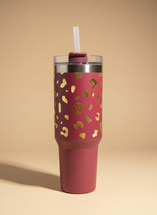 Pink tumbler with gold leopard print held by a person inside a vehicle.